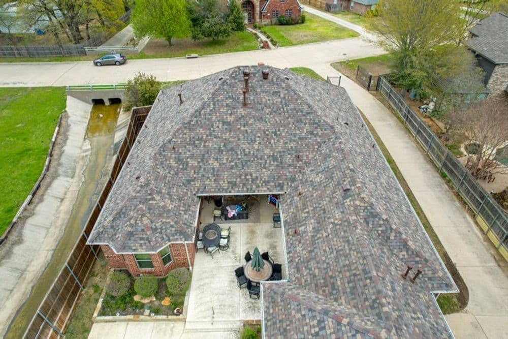 Aerial view of a home with a stone roof and patio surrounded by lush greenery.