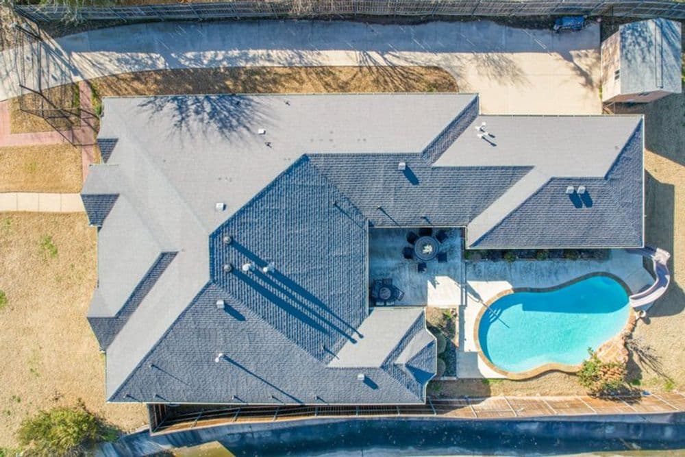 Aerial view of a modern home with a pool and landscaped yard in a sunny neighborhood.