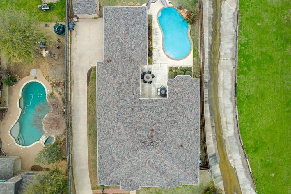 Aerial view of a house with a pool, patio area, and green lawn surrounding it.