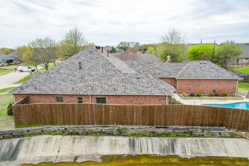 Aerial view of a brick house with a fenced backyard and swimming pool on cloudy day.