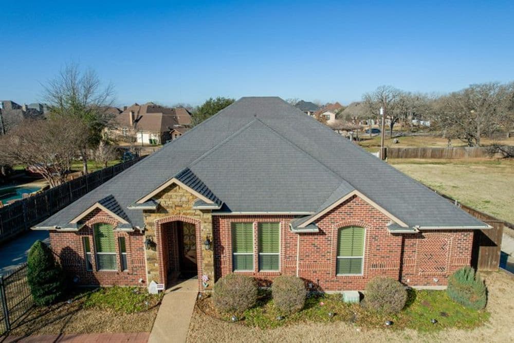 Red brick house with a gray roof, surrounded by landscaped greenery and a spacious yard.