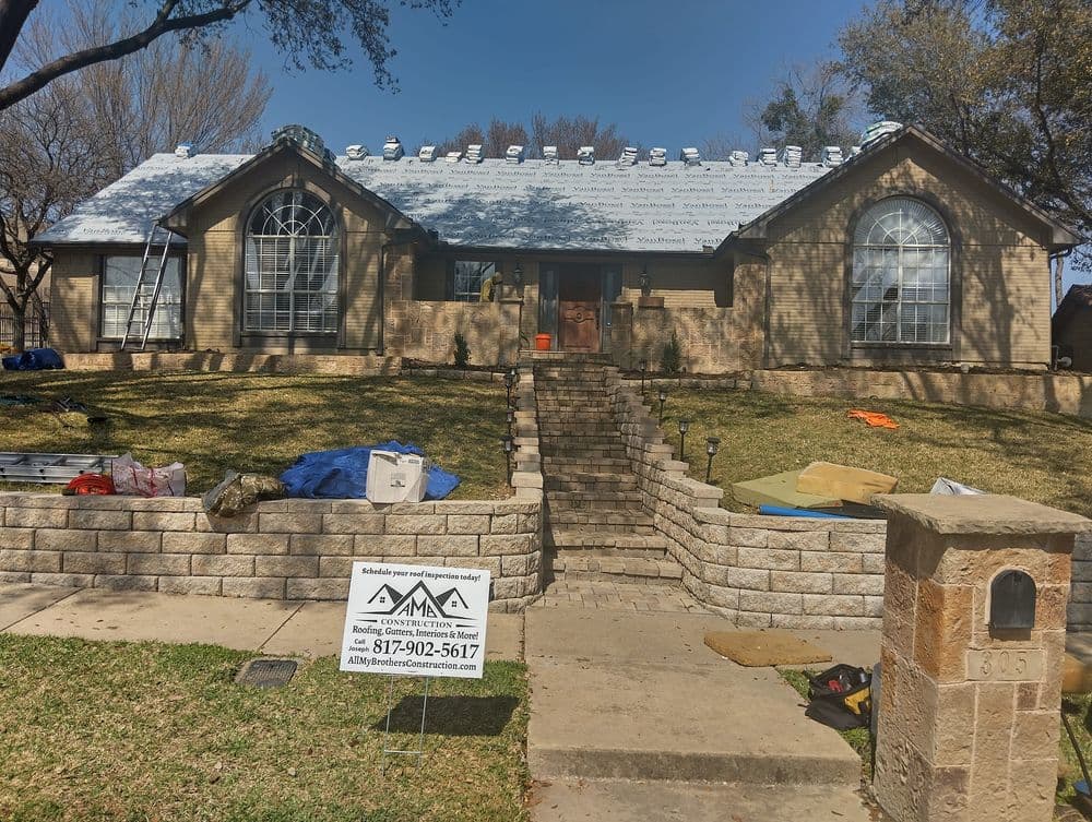 House undergoing roofing work with materials, tools, and a sign for a roofing company in front.