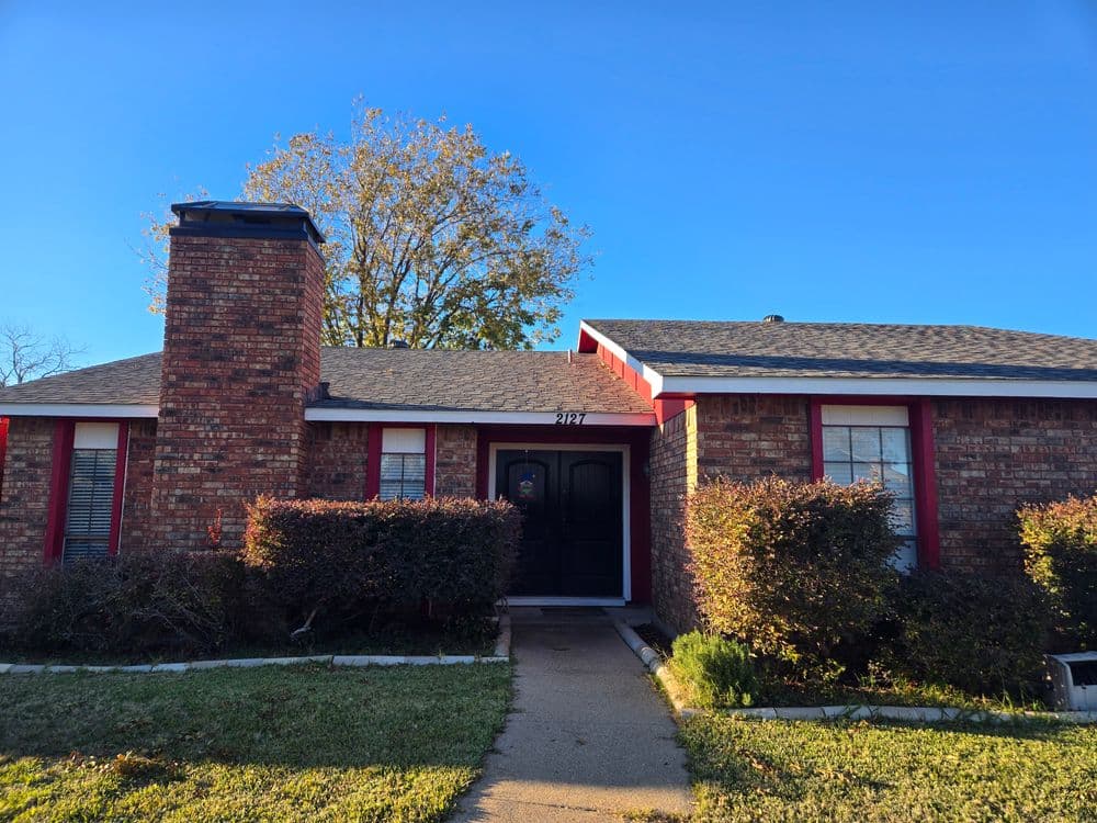 Red brick house with a chimney, black front door, and well-kept landscaping.