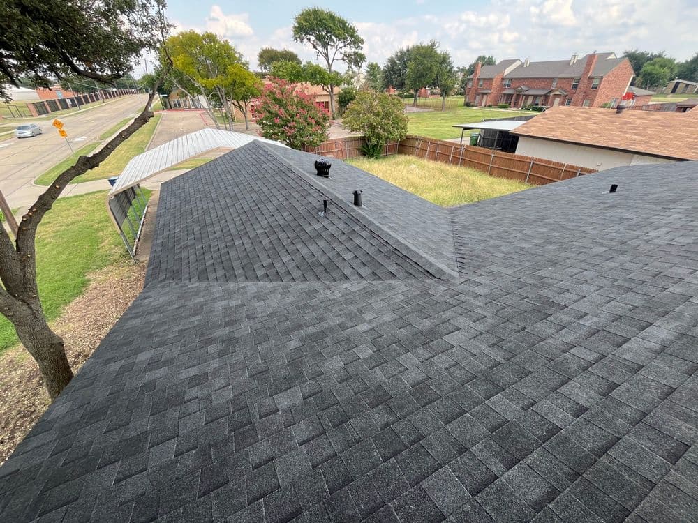 Aerial view of a newly shingled black roof on a suburban house. Green trees and homes in background.