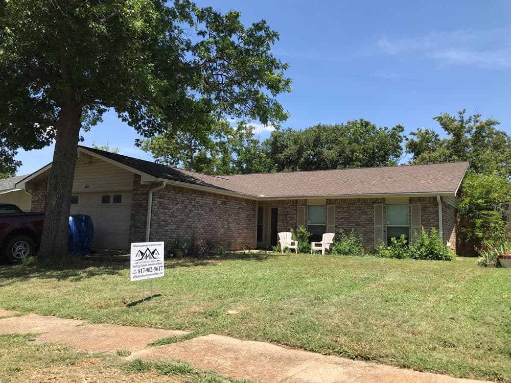 Single-story brick house with a front yard, chairs, and a for-sale sign. Clear blue sky.